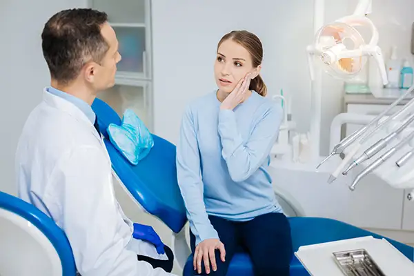 Concerned white patient discussing her tooth pain with her dentist while sitting in a dental chair
