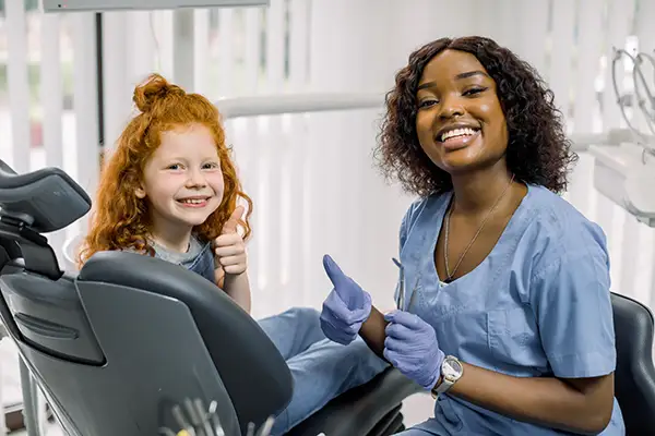 A smiling young girl and her dentist giving thumbs up from the dental chair, in honor of a great back to school checkup at  Cascade Dental in Medford, OR